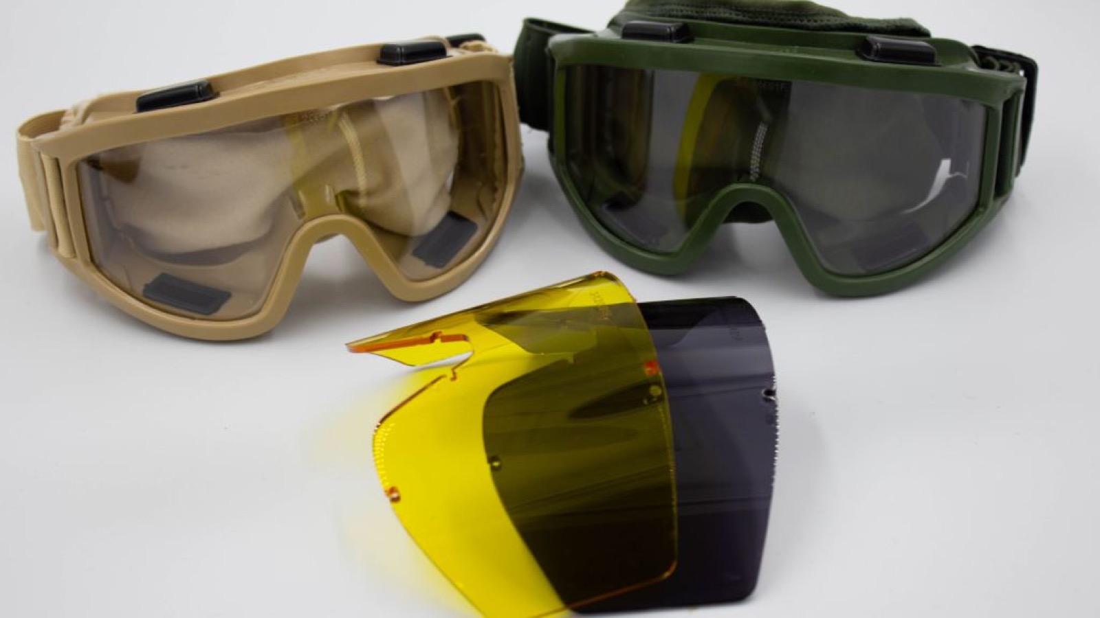 Two pairs of ballistic goggles in tan and green with a spare amber and smoke lens