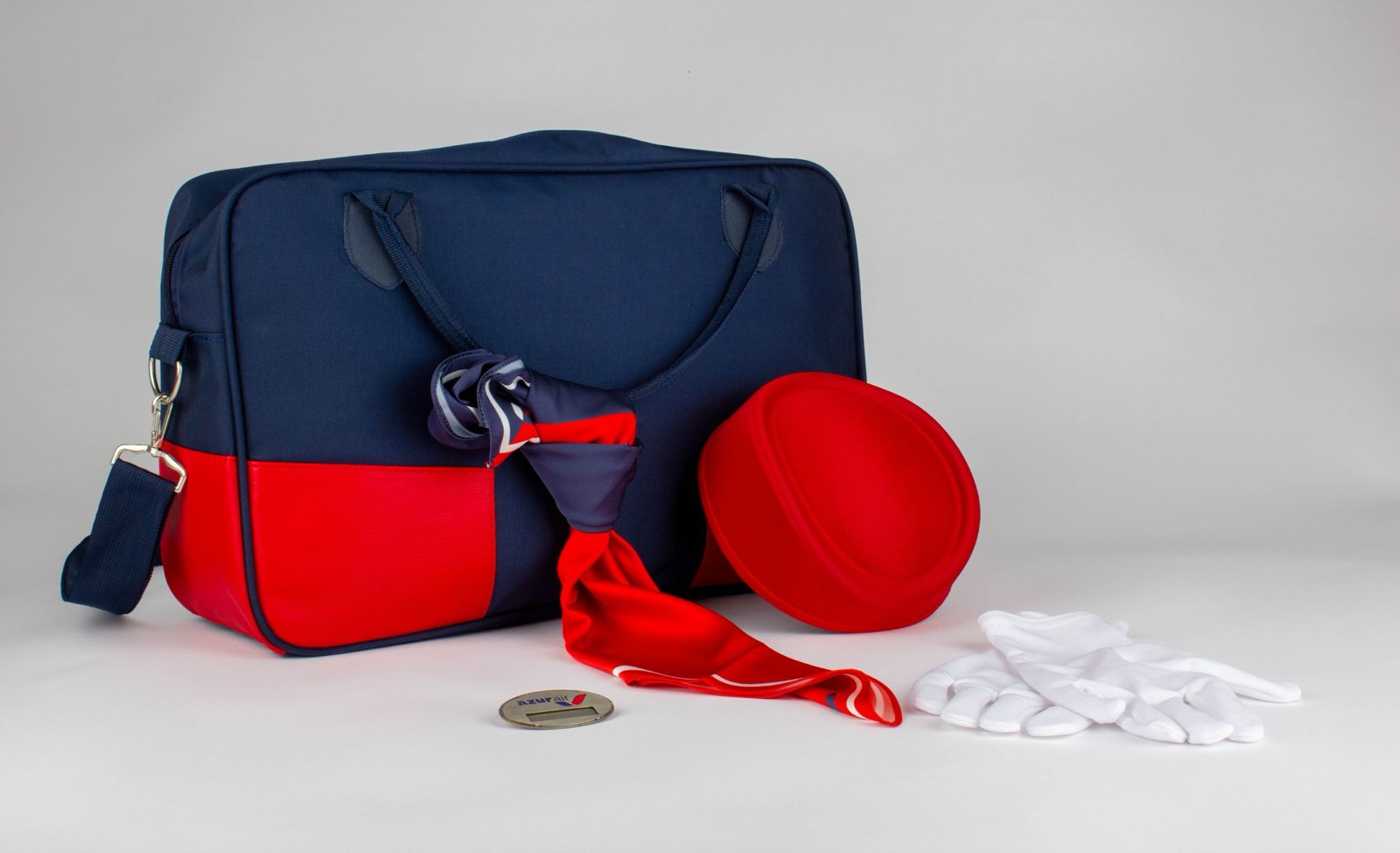 A navy and red flight bag with a matching scarf, red pillbox hat, white gloves, and a wings badge