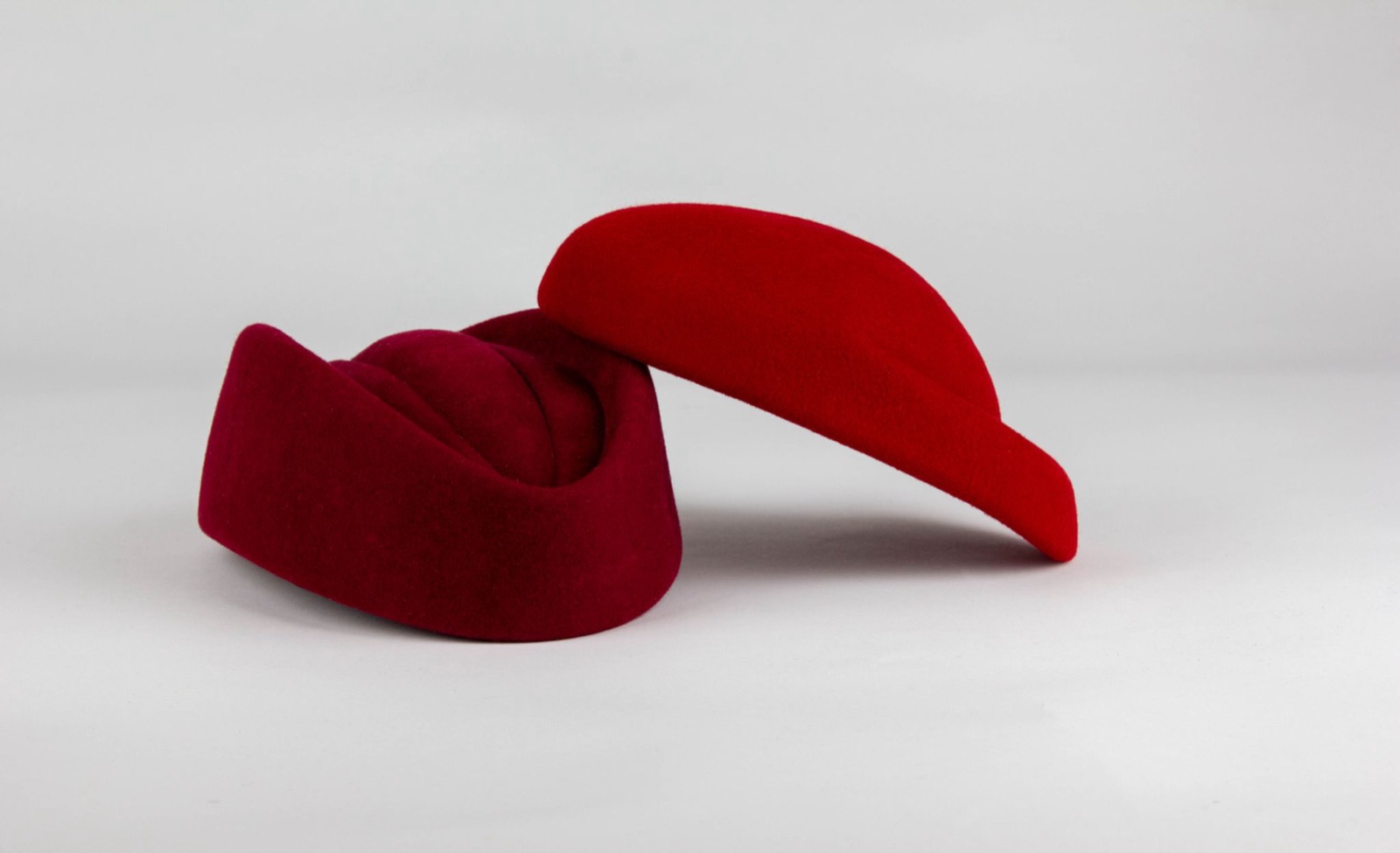 A burgundy and a bright red cabin-crew wool beret on a pale grey surface