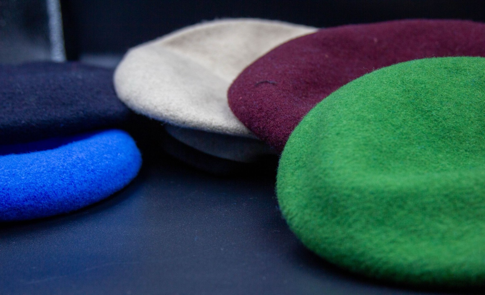 A row of wool military berets in navy, blue, cream, maroon, and green
