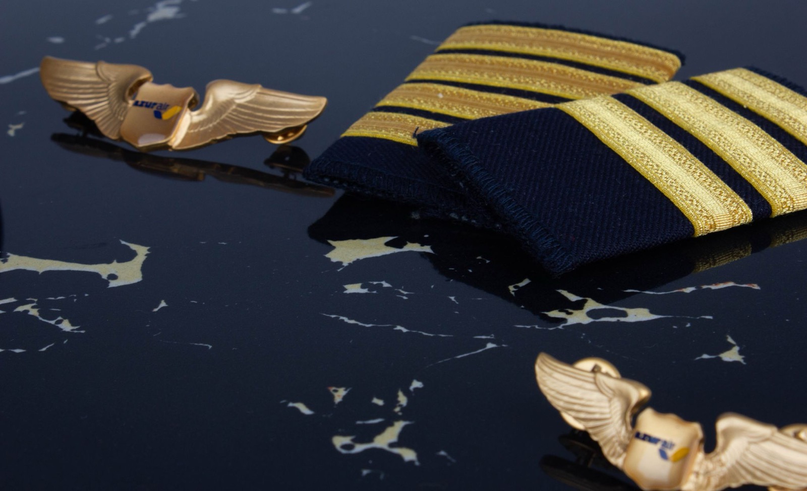 Gold four-bar epaulettes and a gold winged pilot badge on a dark navy surface