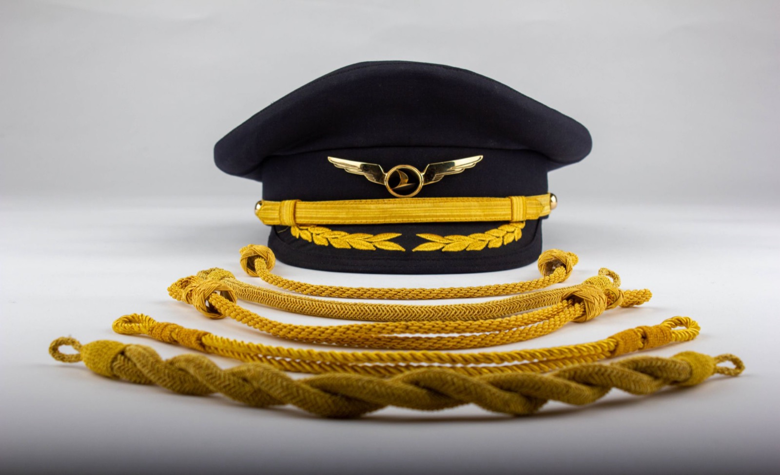 A navy pilot peaked cap with gold oak-leaf braid and winged badge, with gold aiguillette cords in front