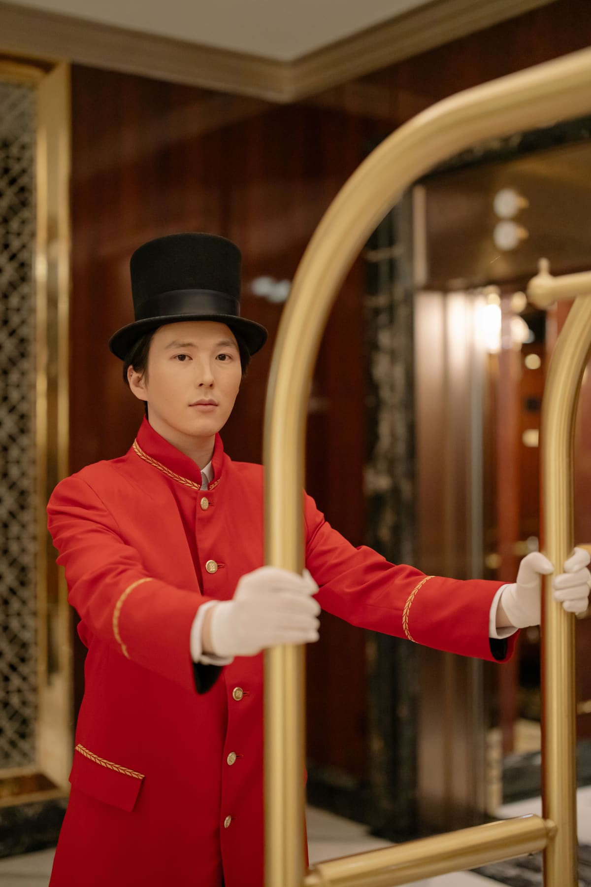 A hotel bellhop in a red gold-braided uniform and top hat with a luggage cart