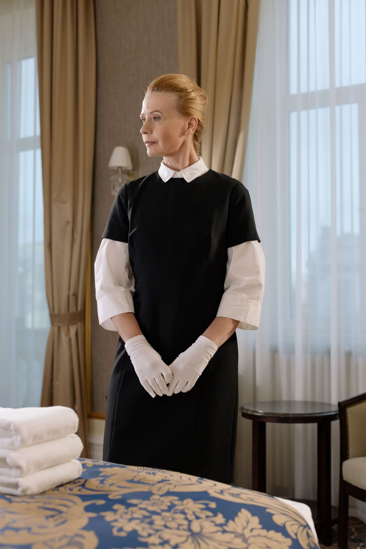 A hotel housekeeper in a black and white uniform folding towels in a guest room